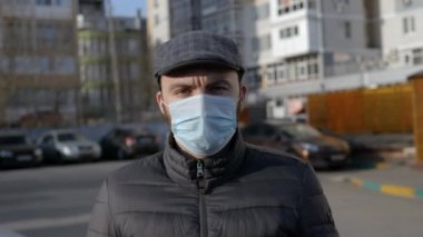 Tıbbi maskeli sakallı adam kameraya bakıyor..