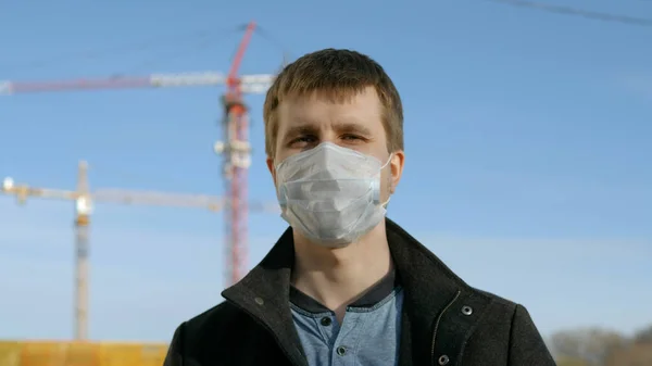 Hombre adulto con máscara médica de pie junto a la construcción sentarse —  Fotos de Stock