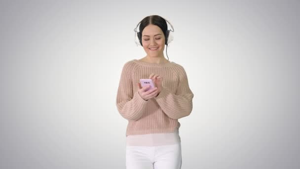 Gelukkig meisje lopen luisteren naar muziek met smart phone dragen hoofdtelefoon op gradiënt achtergrond. — Stockvideo