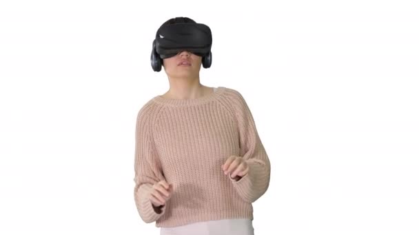 Linda mujer joven caminando y usando auriculares VR interactivos sobre fondo blanco. — Vídeos de Stock