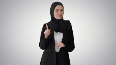 Kendine güvenen genç Müslüman iş kadını tesettürlü giyiniyor ve gradyan arkaplanda kameraya hitap ediyor.