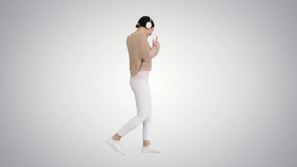 Happy emotional girl listening to music via white headphones and walking on gradient background. — Stock Video