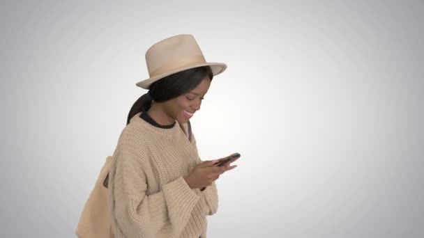 Donna afroamericana in cappello, messaggi sul cellulare sorridenti su sfondo sfumato . — Video Stock