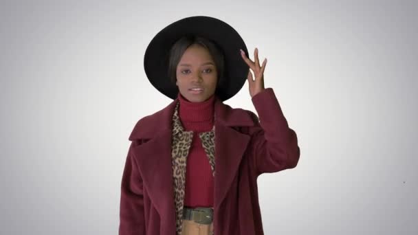 Lindo modelo afro en abrigo tocando sombrero caminando sobre fondo degradado . — Vídeo de stock