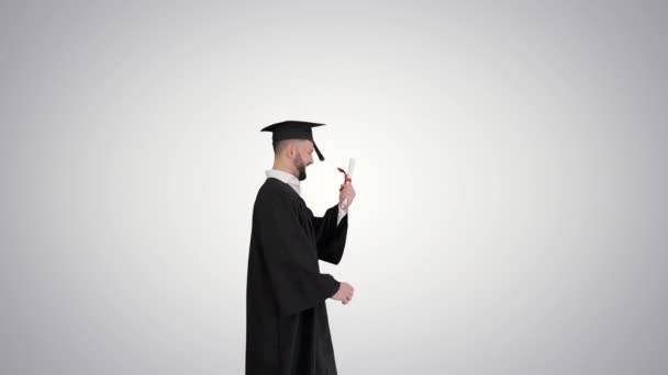 Feliz y emocionado graduado estudiante masculino lanza sombrero en el aire en el fondo gradiente . — Vídeo de stock