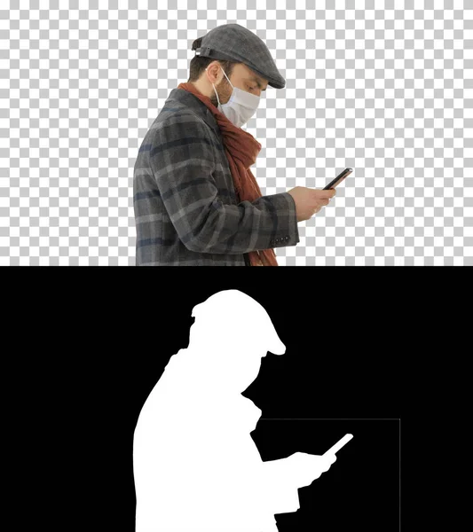 Κομψός άνθρωπος με ιατρική μάσκα περπατώντας και χρησιμοποιώντας έξυπνο τηλέφωνο, Alpha — Φωτογραφία Αρχείου