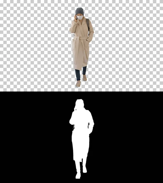 Mladá žena v ochranné masce chůze a mluvení mobilním pho — Stock fotografie