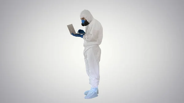 Médico em uniforme de proteção branco usando laptop em fundo gradiente . — Fotografia de Stock