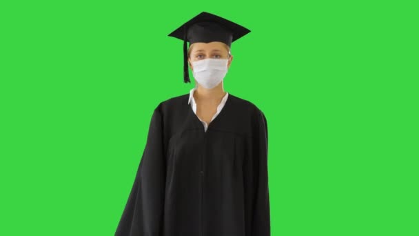 Жіночий випускник у капюшоні та сукні, який носить медичну маску, йдучи на зеленому екрані, Chroma Key. — стокове відео