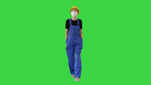 Young woman in yellow hardhat and in medical mask walking on a Green Screen, Chroma Key. — Stock Video