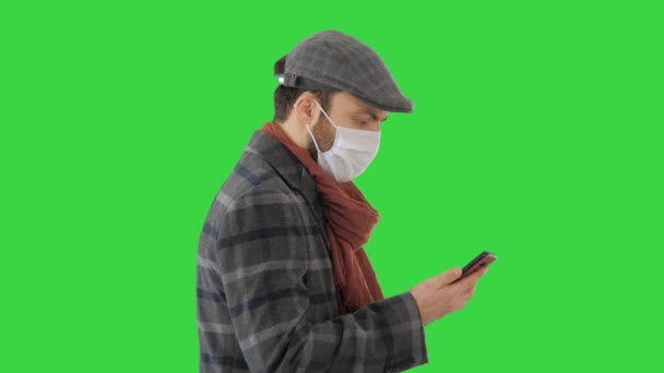 Dorosły mężczyzna nosi ochronną maskę medyczną rozmawiając przez telefon i spacerując po zielonym ekranie, Chroma Key. — Wideo stockowe
