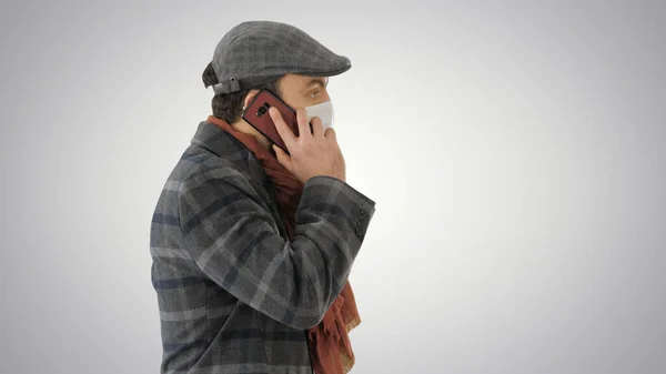 大人の男は電話で話して保護医療マスクを身に着けているとグラデーションの背景に歩いて. — ストック写真
