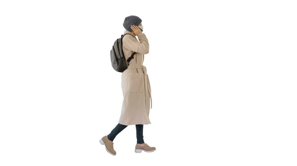 Vrouw draagt medisch masker lopen en bellen iemand een van de telefoon op witte achtergrond. — Stockfoto