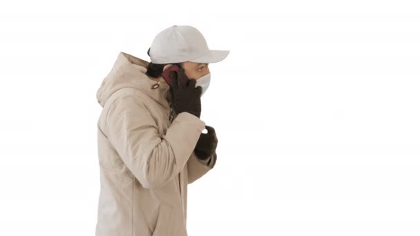 Homem usa máscara médica protetora e fala ao telefone andando sobre fundo branco . — Vídeo de Stock