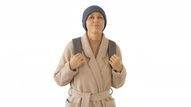 コートとバックパックを着て白い背景を歩く若い女性. — ストック動画