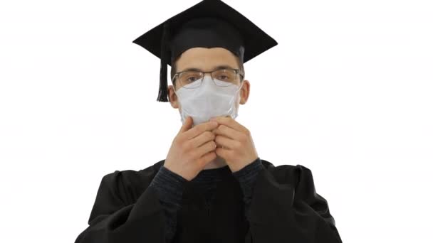 Jeune homme avec robe de remise des diplômes en masque médical sur fond blanc . — Video