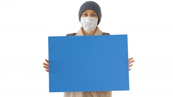 Femme en vêtements de plein air et en masque médical tenant le tableau blanc sur fond blanc . — Video