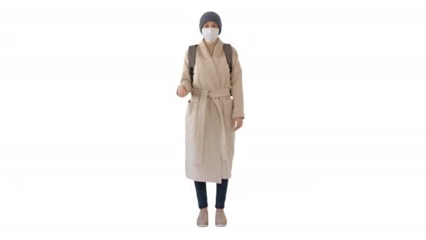 Κορίτσι σε μια ιατρική μάσκα προσώπου στέκεται σε ένα παλτό σε λευκό φόντο. — Αρχείο Βίντεο