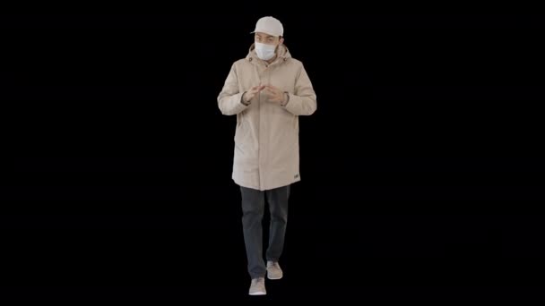 Muž v zimním oblečení a lékařská maska mluví s vámi něco vysvětlovat při chůzi, Alpha Channel — Stock video