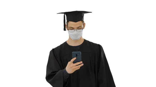 Giovane studente raduate in maschera medica utilizzando telefono a piedi su sfondo bianco . — Foto Stock