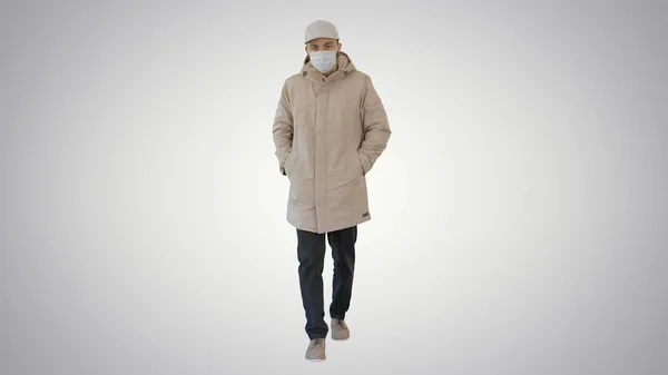 Homem de casaco quente andando e colocando máscara médica no fundo gradiente . — Fotografia de Stock