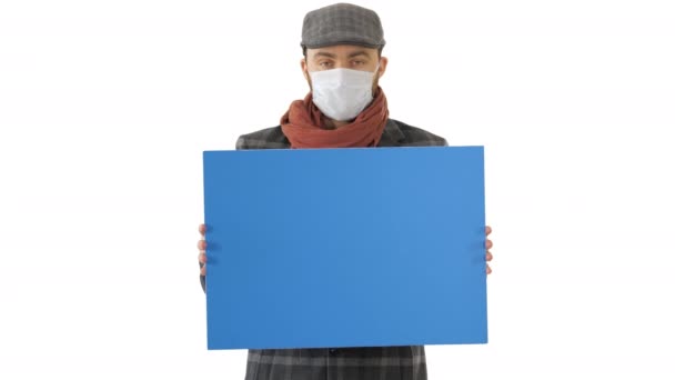 Man i en trendig outfit och medicinsk mask håller tomma plakat på vit bakgrund. — Stockvideo