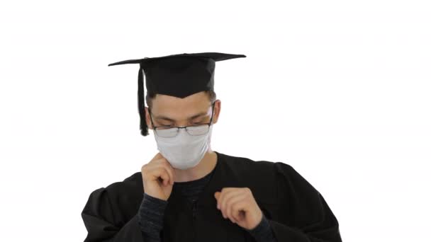 Student in gaduation jurk en gezichtsmasker struikelen over witte achtergrond. — Stockvideo