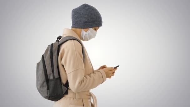 Orvosi maszkot viselő nő, aki gradiens alapon jár. — Stock videók