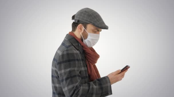 Hombre adulto lleva máscara médica protectora hablando por teléfono y caminando sobre el fondo gradiente . — Vídeos de Stock