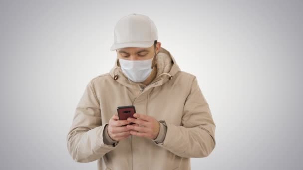 Young casual man walking making a call wearing warm clothes and protective mask on gradient background. — Stock Video