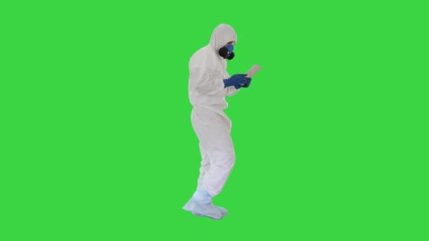 Bilimadamı ya da doktor biyo-tehlike giysileri ve koruyucu maskeler giyip yeşil ekranda yürürken dijital tablet kullanıyor.. — Stok video