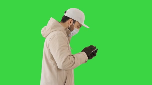 Kaukasischer Mann mit medizinischer Maske beim Gehen und Telefonieren auf einem Green Screen, Chroma Key. — Stockvideo