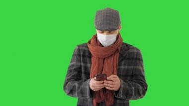 Tıbbi maskeli adam telefon kullanıyor ve yeşil ekranda yürüyor, Chroma Key..