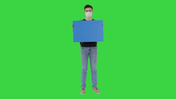 Orvosi maszkos diák üres matricával a kezében a zöld vásznon, Chroma Key. — Stock videók