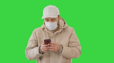 Genç sıradan bir adam yeşil ekranda kalın giysiler ve koruyucu maske takarak arama yapıyor, Chroma Key.
