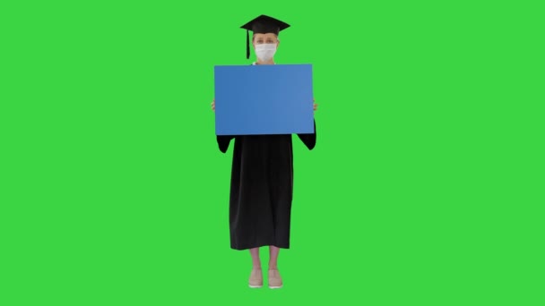 Απόφοιτος φοιτητής κορίτσι με μάσκα προστασίας κρατώντας κενό πίνακα σε μια πράσινη οθόνη, Chroma Key. — Αρχείο Βίντεο