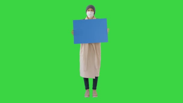 Femme en vêtements de plein air et en masque médical tenant le tableau blanc sur un écran vert, Chroma Key . — Video