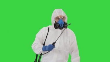 Koruyucu üniformalı bir virüs uzmanı yeşil ekranda bölgeyi dezenfekte ediyor..