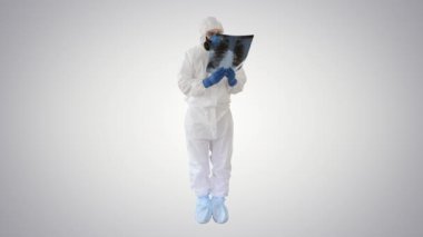Koruyucu antibakteriyel giysi ve tıbbi maske giyen bulaşıcı hastalıklar doktoru Pulmonolog, arka plandaki akciğerlerin röntgenini inceliyor..