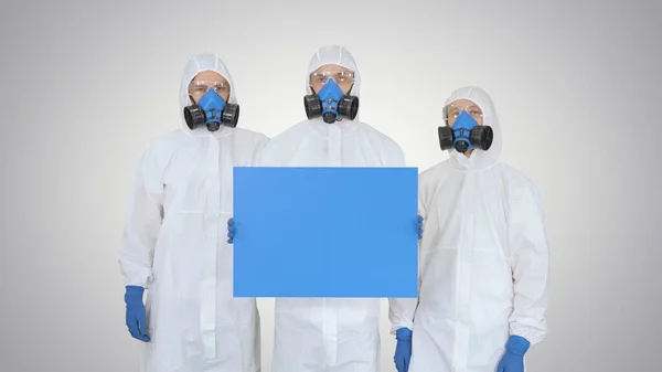 Tres doctores en trajes protectores sosteniendo tablero en blanco sobre fondo degradado . —  Fotos de Stock