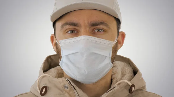 Chory młody człowiek przystojny nosząc medyczną maskę na gradientowym tle. — Zdjęcie stockowe