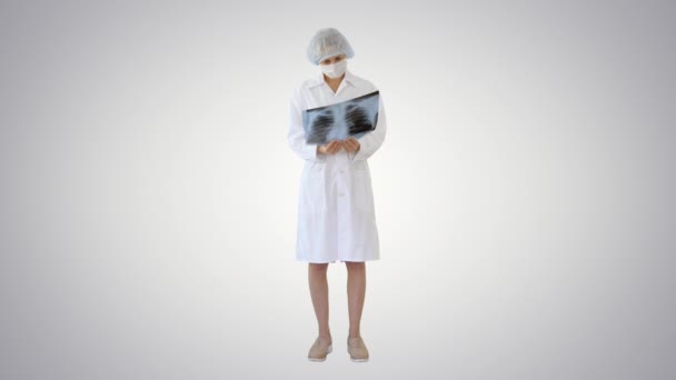 Femme médecin en masque regardant la radiographie pulmonaire sur fond de gradient . — Video