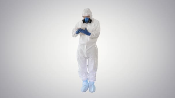 Male doctor in protective suit using digital tablet on gradient background. — Stock Video