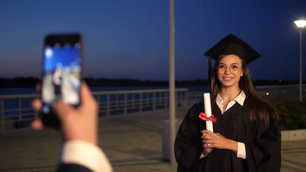 Glimlachende vrouwelijke afgestudeerde student wordt gefotografeerd door haar vriend. — Stockfoto