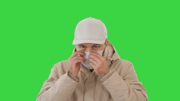 Mann im warmen Mantel, der auf einem Green Screen eine medizinische Maske aufsetzt, Chroma Key. — Stockvideo