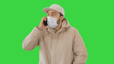 Avrupalı genç adam arıyor yüzünde tıbbi bir maskeyle yeşil ekranda, Chroma Key.