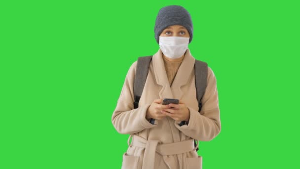 Frau in einem Mantel mit medizinischer Maske mit Telefon und Fuß auf einem Green Screen, Chroma Key. — Stockvideo