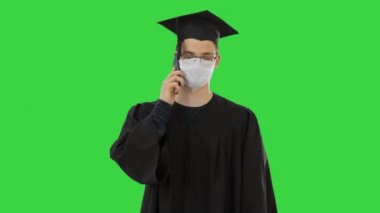 Genç lisansüstü öğrencisi, yeşil ekranda tıbbi maskeli akıllı telefonuyla Chroma Key kullanıyor..