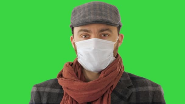 緑の画面上に使い捨ての保護顔マスクを身に着けている流行のコートでハンサムな若いヨーロッパ人、クロマキー. — ストック動画