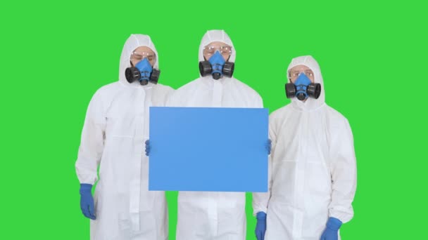 Drie artsen in beschermende pakken houden blanco boord op een groen scherm, Chroma Key. — Stockvideo